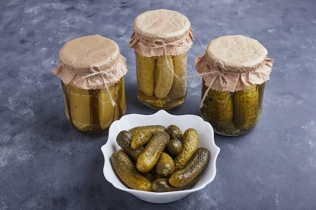 Бесплатное фото Маринованные огурцы в миске и стеклянных банках на синей поверхности.